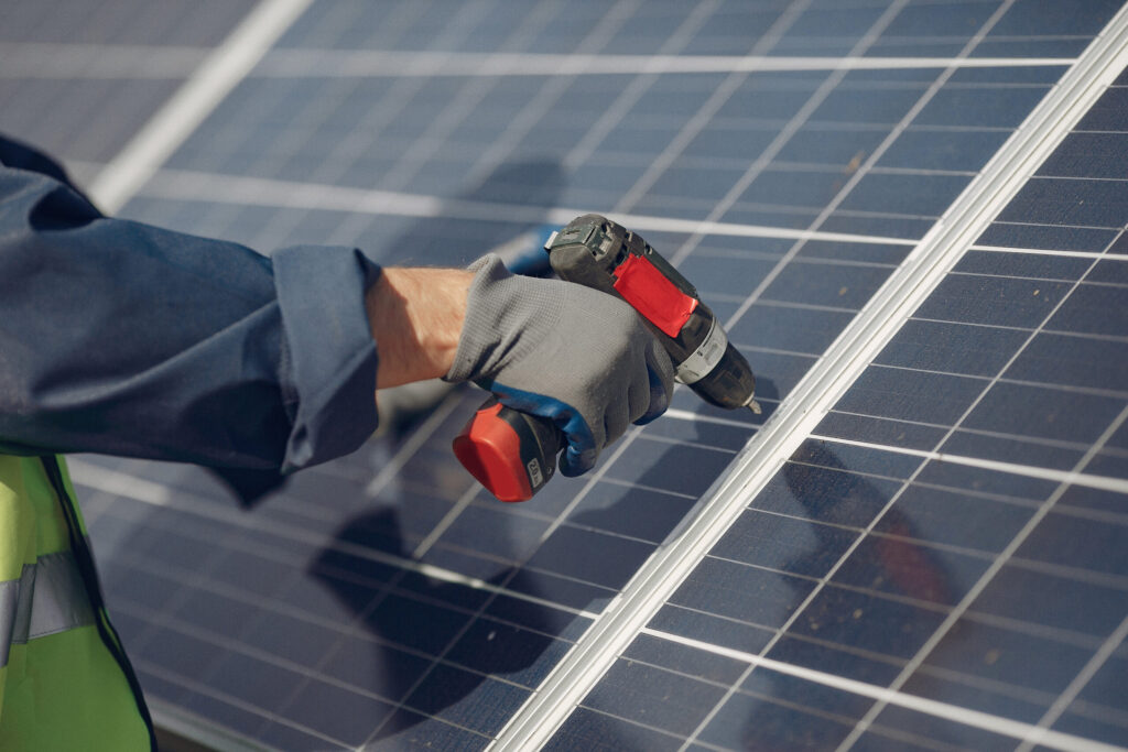 A close-up of a gloved hand operating a drill on a solar panel, focusing on installation work.
